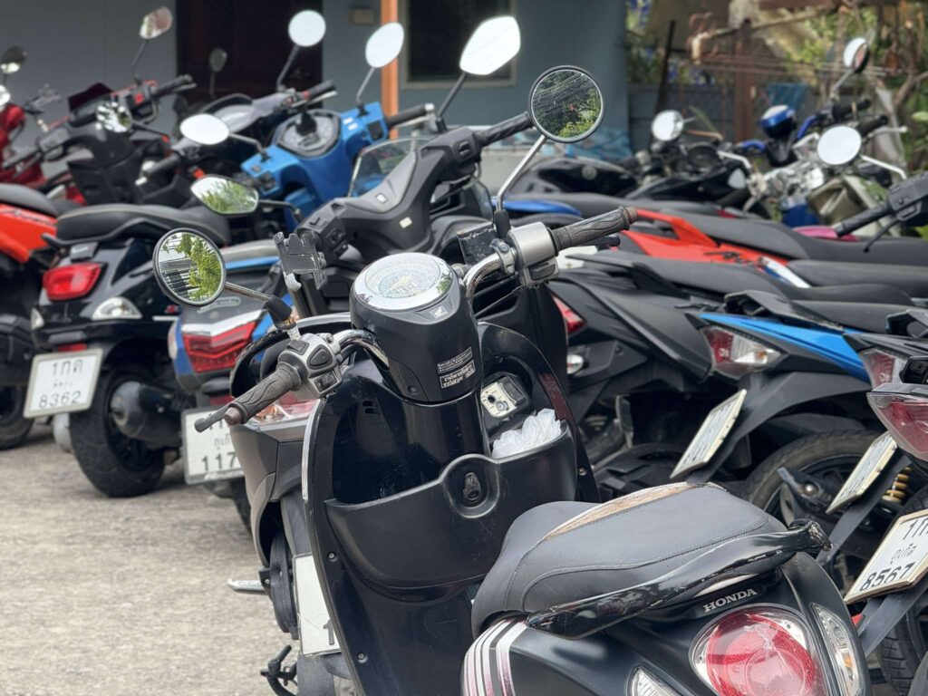 "Promotional poster for Ton Car Rent Phuket featuring EV and scooter rentals. Aion U electric car and Honda Scoopy scooter displayed with a tropical beach background. Text highlights rental prices: EV from 1,000–1,200 THB per day or 18,000–26,000 THB per month, scooters from 150 THB per day or 2,000–5,000 THB per month. Includes free airport delivery and no deposit required."